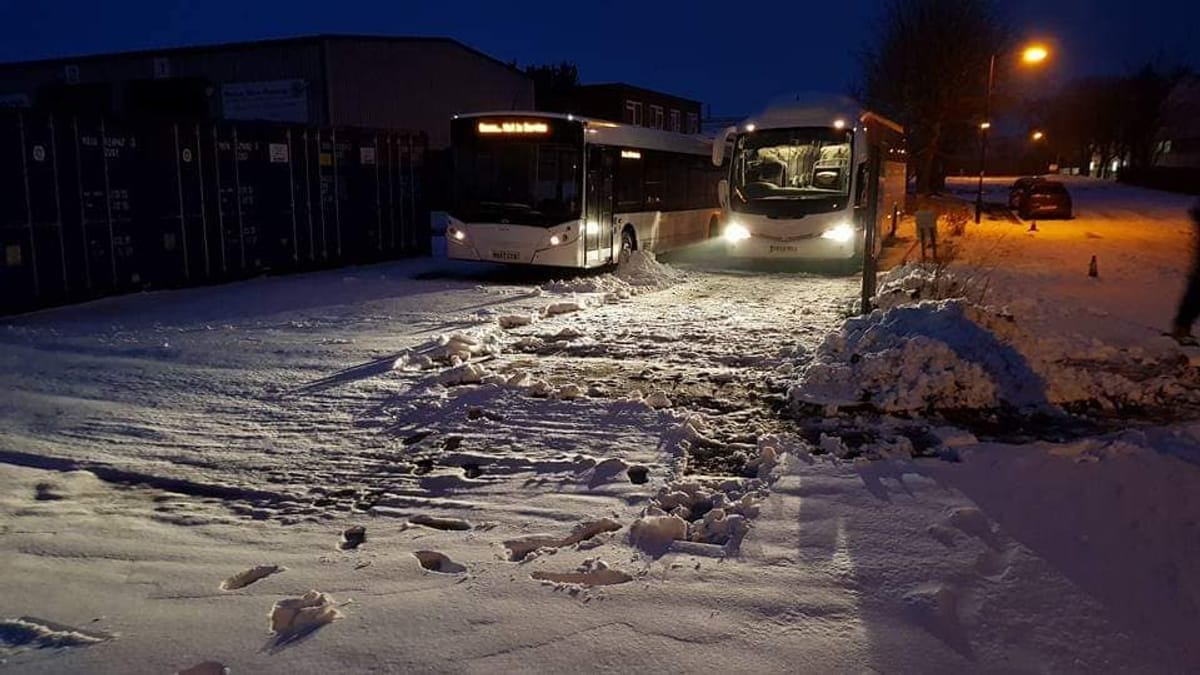 Buses at a depot in the snow before dawn.